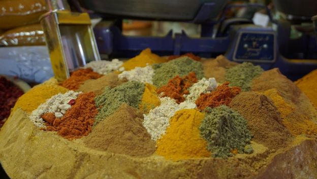 An array of loose spices used in Persian cuisine. A metal measuring scoop is in the background, for doling out the spices.