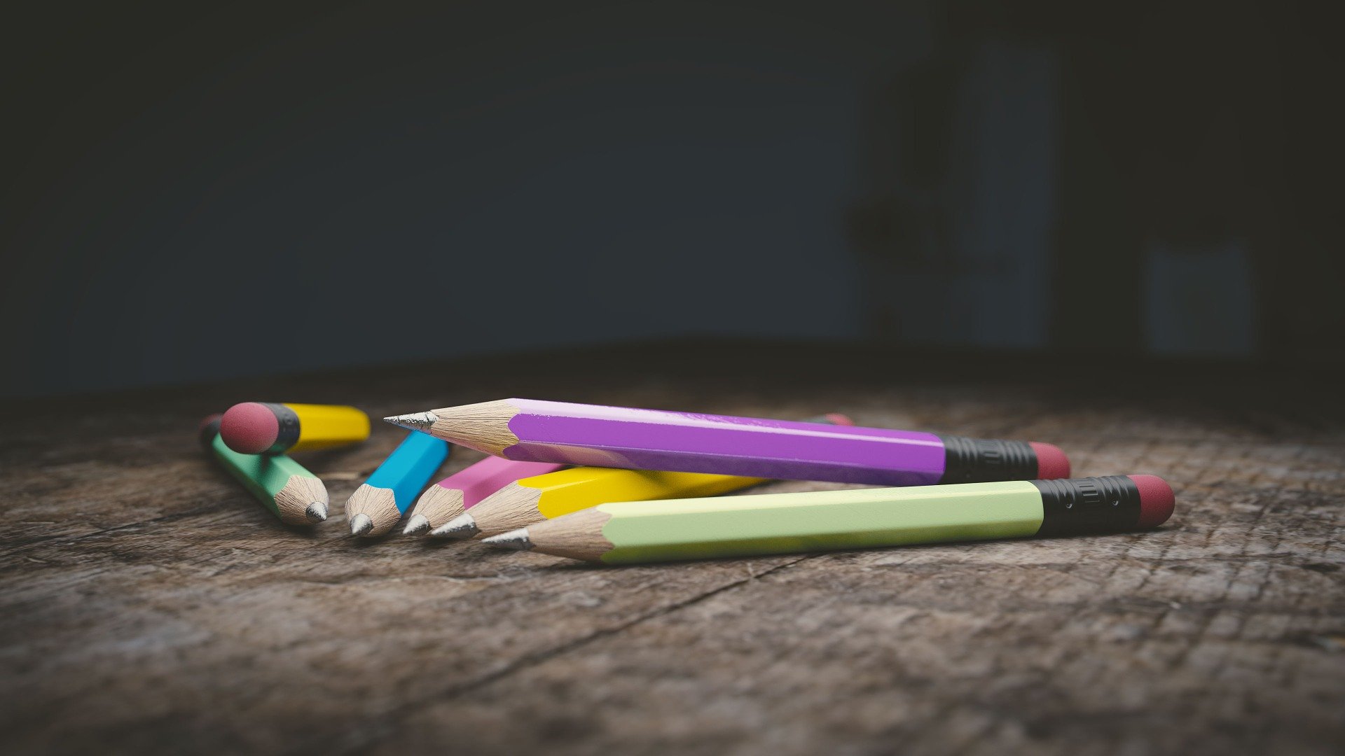 Seven brightly colored pencils lying on a desk.